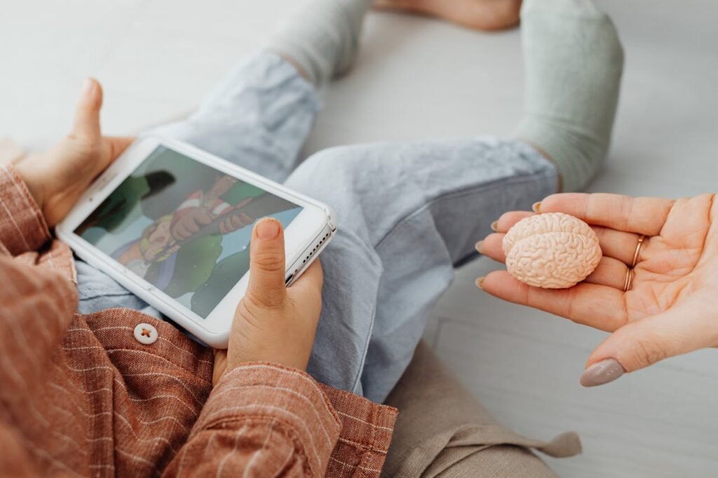 Egy kamasz gyerek tableten filmet néz, miközben egy anyai kéz egy agyat formázó műanyagot nyújt felé. A kép a képernyőidő és a gyermek agyi fejlődése közötti egyensúly fontosságát jelképezi.